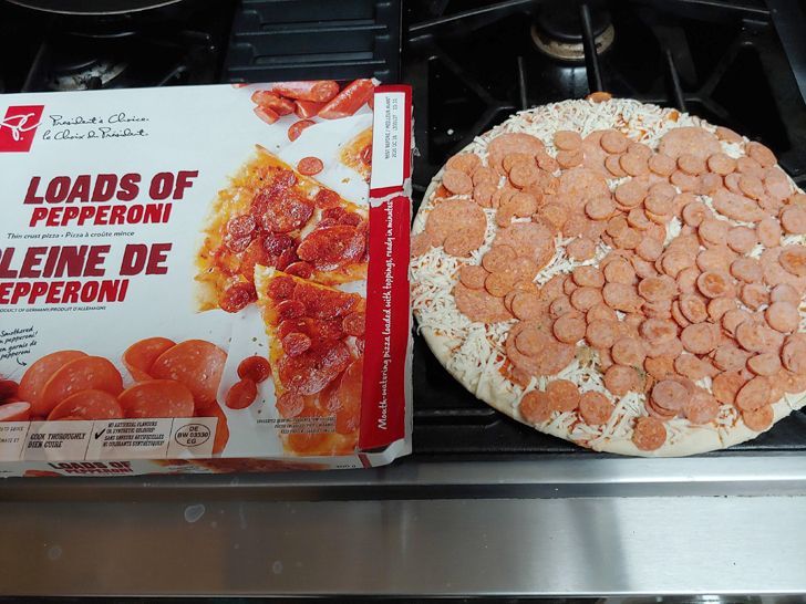 A pepperoni fronzen pizza on the side of its box, both on top of an oven.