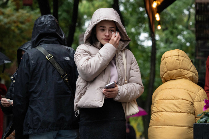 A young woman in a beige puffer jacket wiping off a tear outside.