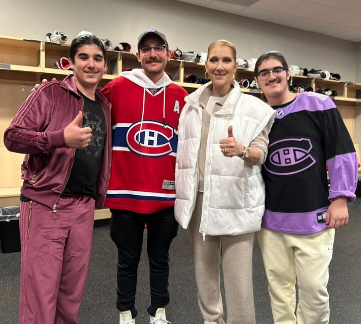 Celine Dion poses for a picture with her thumb up together with three man.
