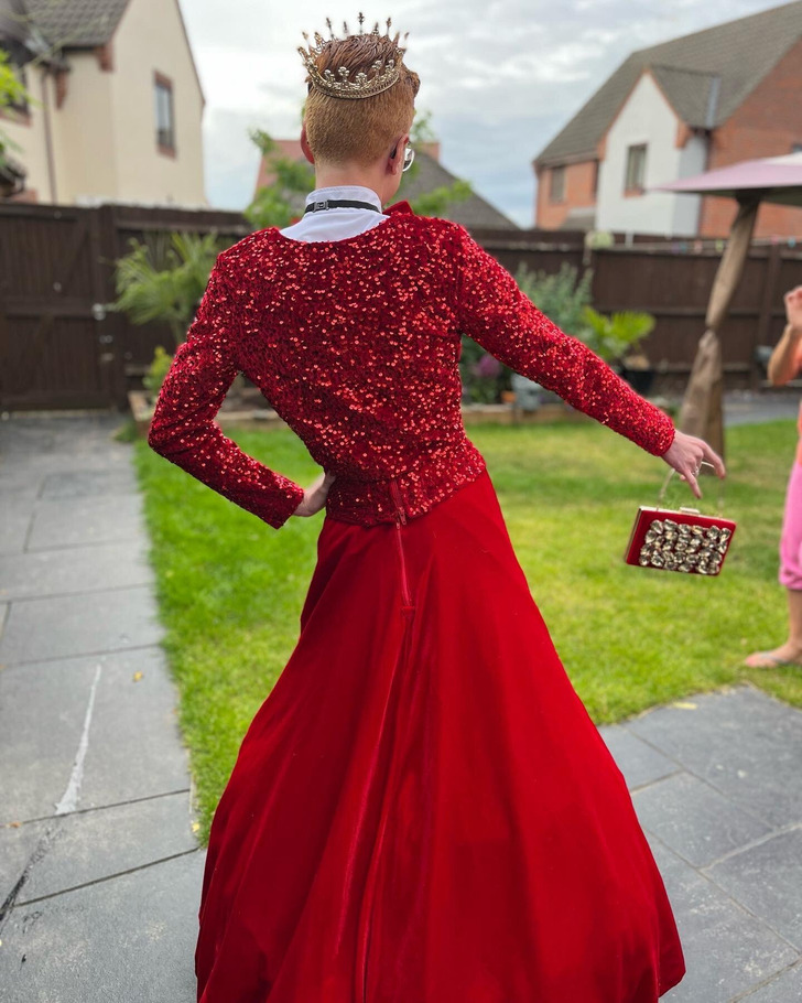 Boy wears a crown and a red gown for prom.