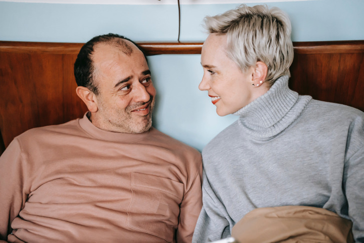 An middle-aged couple looking at each other while in bed.