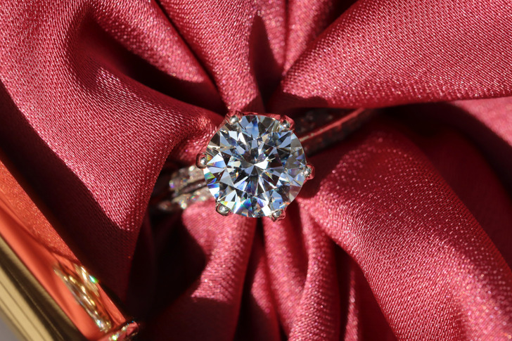 Closeup of a diamond ring with a red fabric through it.