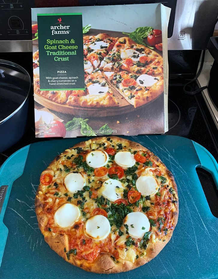 A cooked frozen spinach and goat cheese pizza beside its box.