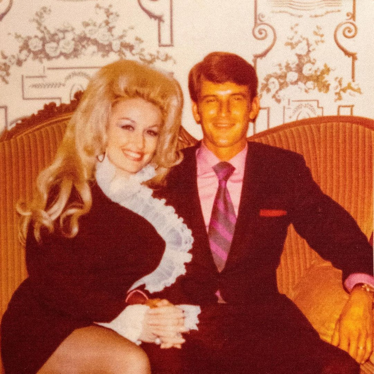 Dolly Parton sitting on a sofa with her husband in their younger days.