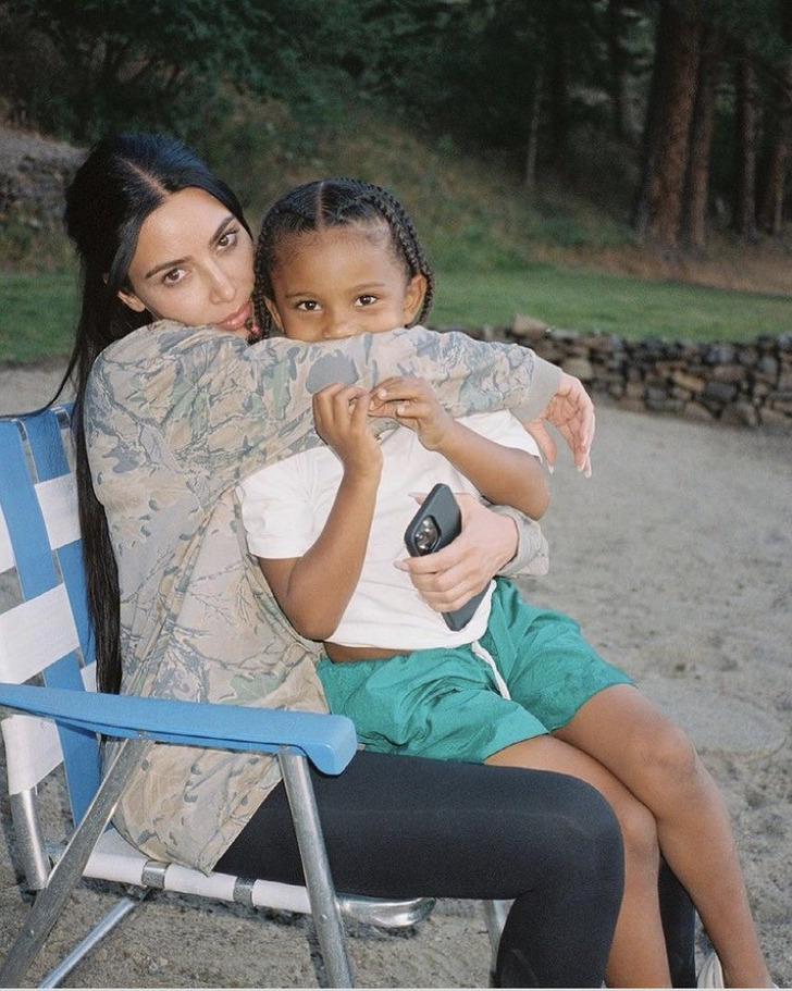 Kim Kardashian in a foldable chair hugging her son outdoors.
