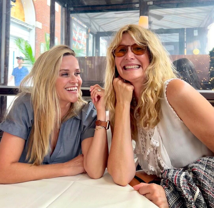 Reese Witherspoon and Laura Dern smile as they sit together in a restaurant.