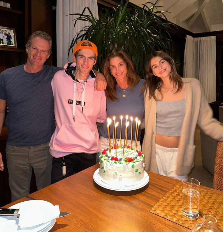 Group photo of Cindy Crawford's family posing in front of a dining table with a cake on it.