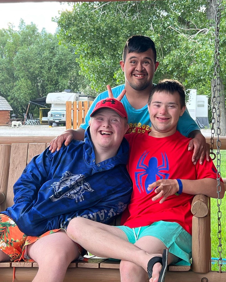 Three young men with Down Syndrome. Two sitting on a bench and the third standing behind them.