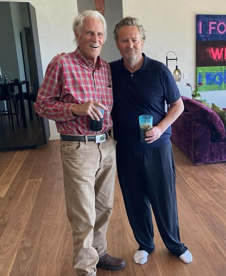 Matthew Perry and an old man standing with their arm around each other holding a beverage.