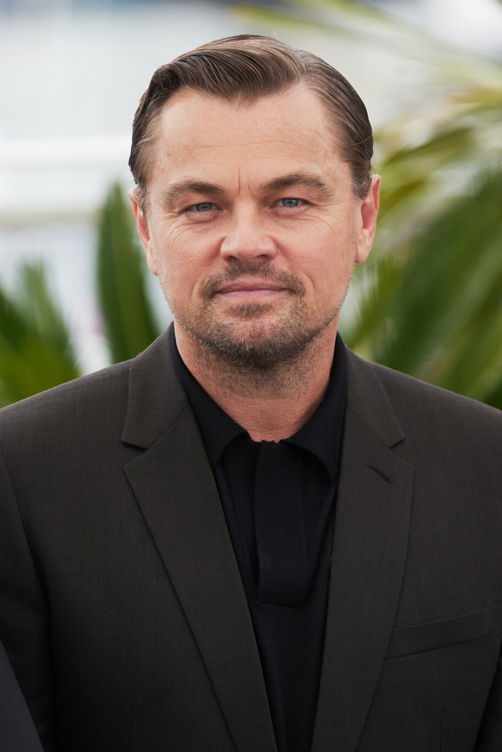 Leonardo DiCaprio looking at the camera wearing a black suit and a black shirt.