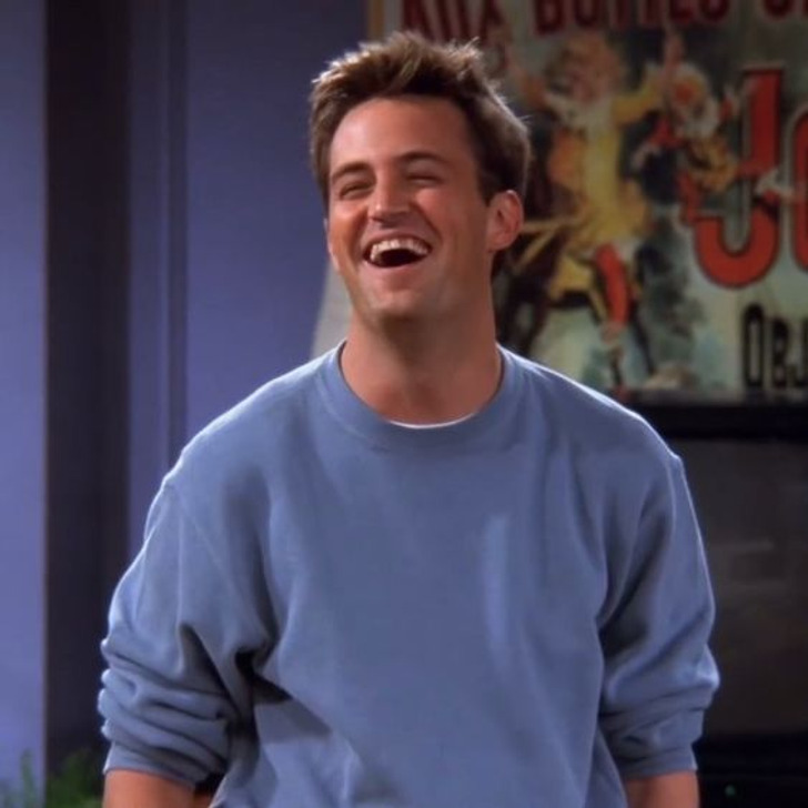 Chandler Bling smiling at Monica's house wearing a blue sweatshirt.