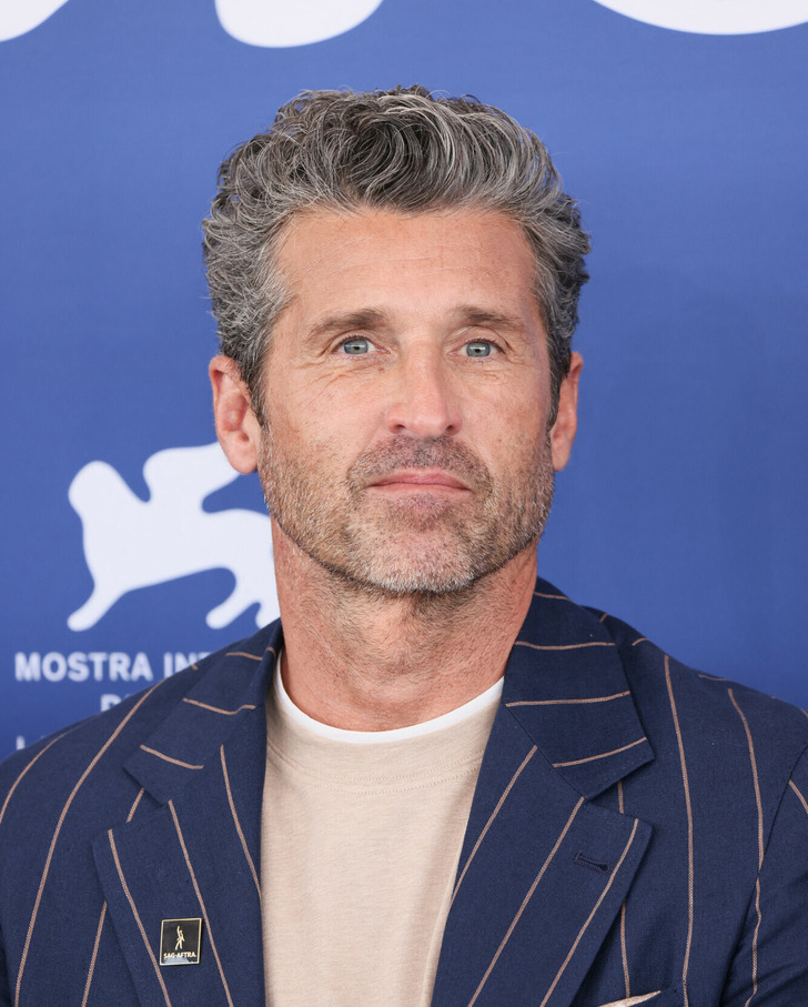 Close up of Patrick Dempsey at an event wearing a blue coat with cream stripes and a cream shirt.