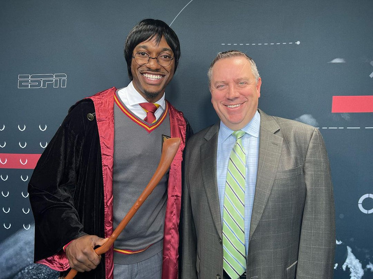 Robert Griffin holding a wand and wearing a cape poses with a man in a suit.