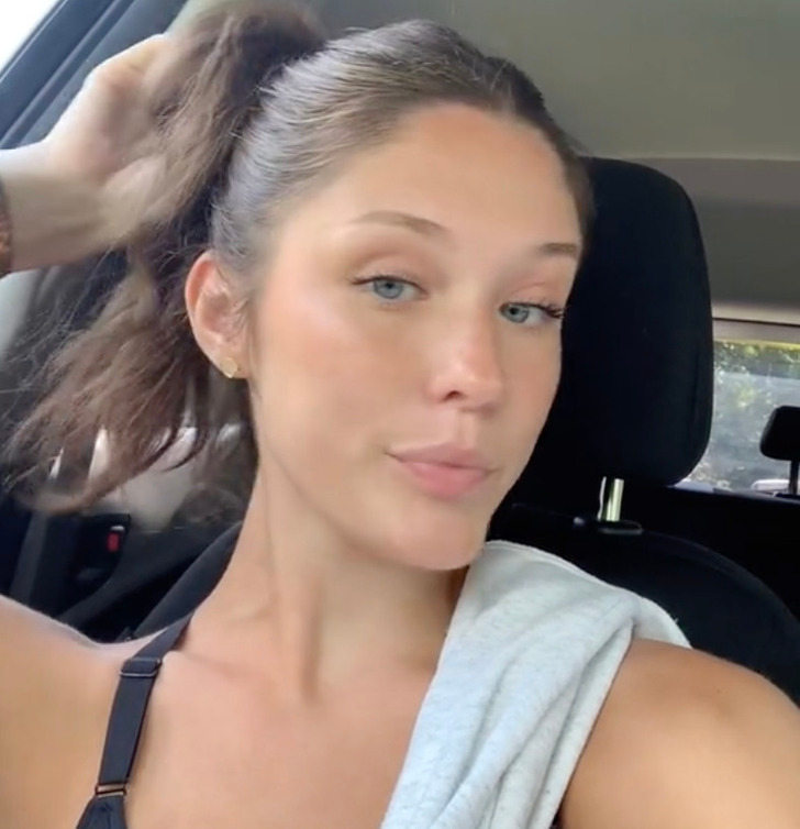 A young woman in a sports bra, blue eyes, looking at the camera, in a car.