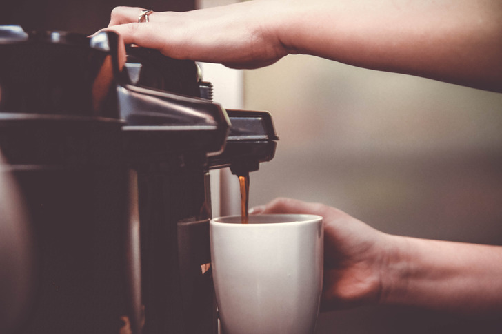 Closeup of a person operating a coffee machine, pouring coffee in a white mug.