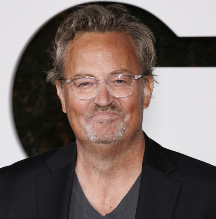 Matthew Perry at the red carpet wearing black suit and grey v-neck t-shirt.