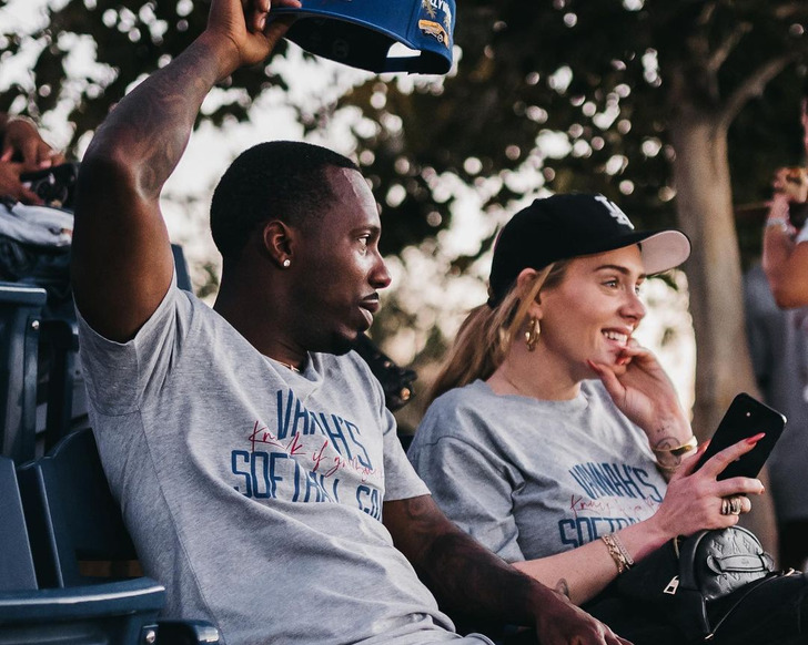 Rich Paul and Adele sitting in chairs outside, smiling, wearing maching grey tshirts.