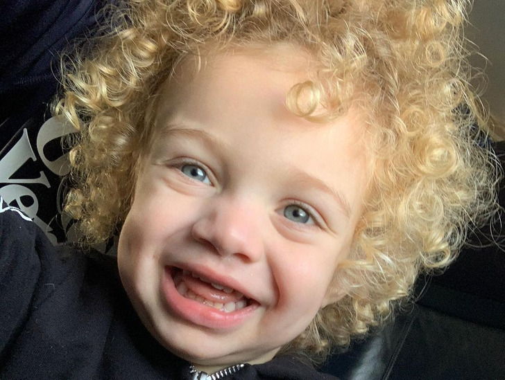 A blond, blue-eyed kid with curly hair smilling.