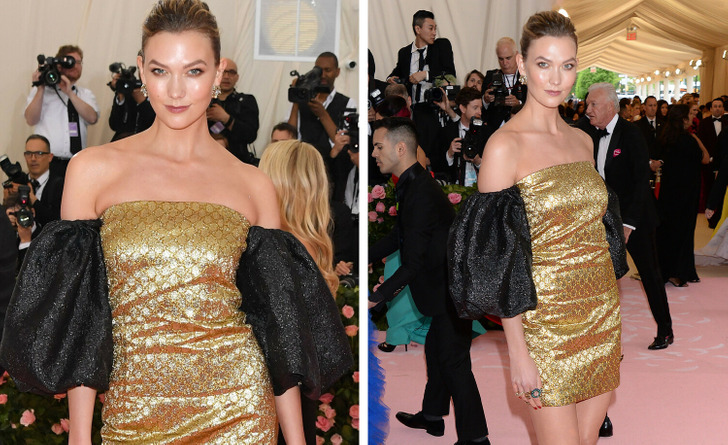 Karlie Kloss poses at an event wearing an off-shoulder golden dress with black puffed sleeves.