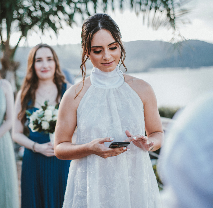 A woman in a white dress looking at a phone, another woman blurred in the background.