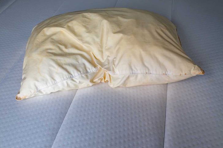 A stained yellow pillow above a mattress.