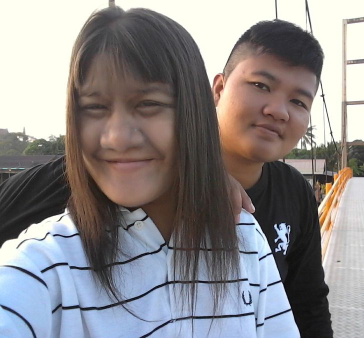 A young couple wearing hoodies posing for a photo on a bridge.