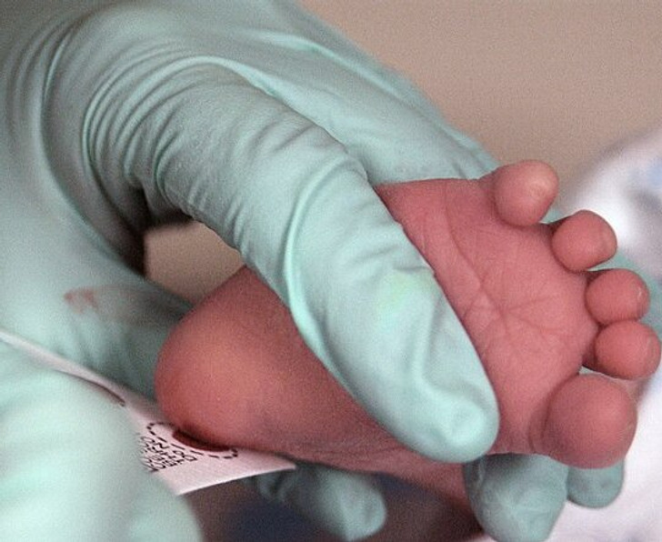 A newborn's feet being held by someone in surgical gloves.