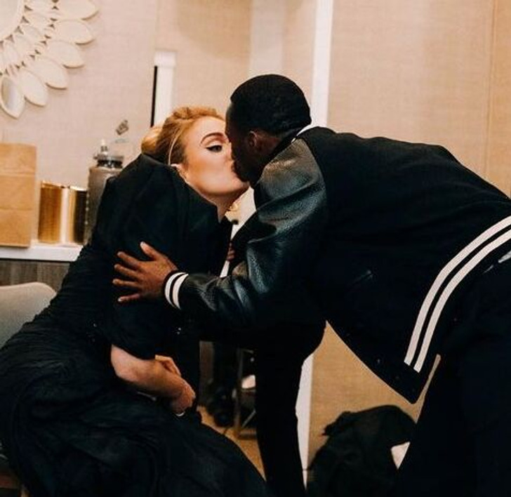 A woman in black gown kissing a man in black varsity jacket.
