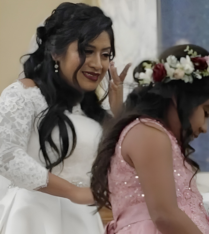 A bride wearing a white gown tearing up together with a kid wearing a pink dress.