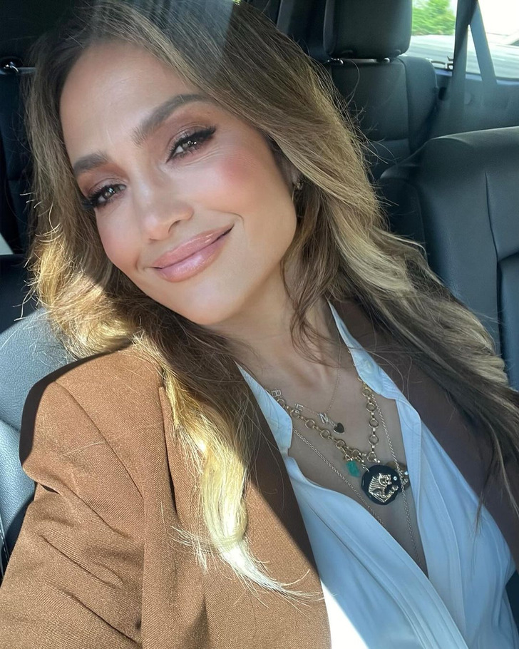 Jennifer Lopez taking a selfie inside a car wearing a brown blazer.