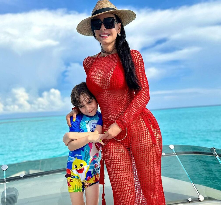 A brunette lady wearing a red dress with her grandson on a boat at the sea.