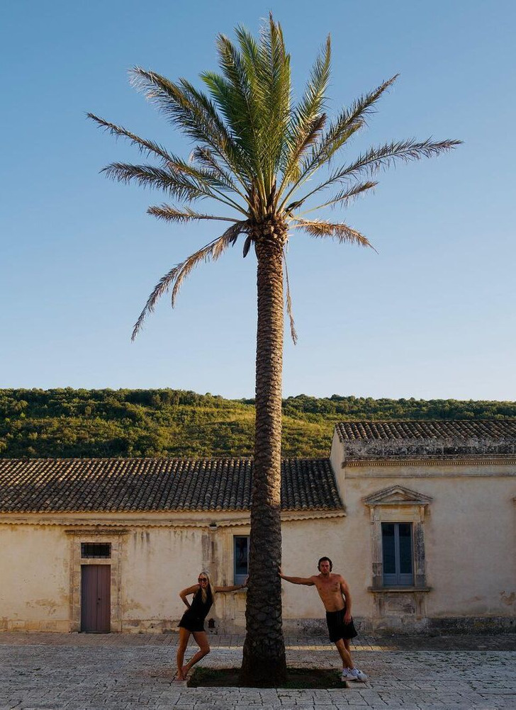 A couple posing beside a giant palm tree, leaning over it.