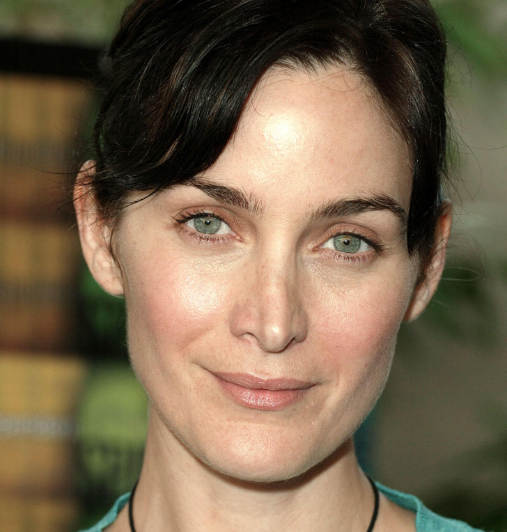 Close-up of young Carrie-Anne Moss looking at the camera, teal ripped top, reflective necklace.