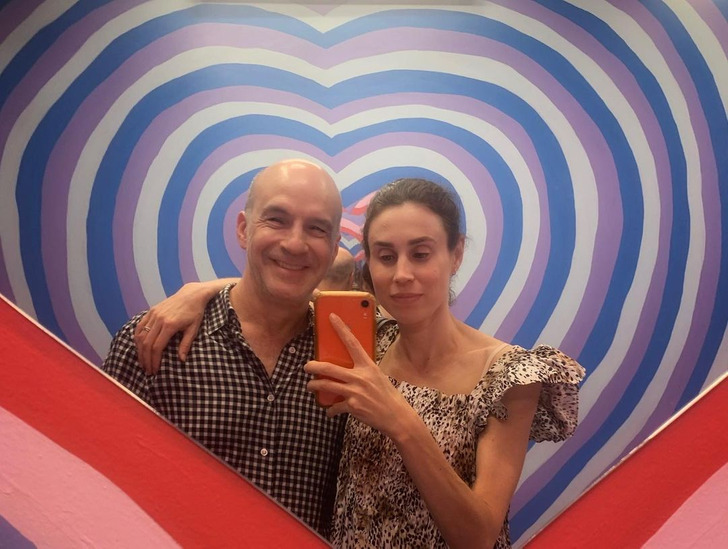 A couple taking a selfie in a heart-shapped mirror.