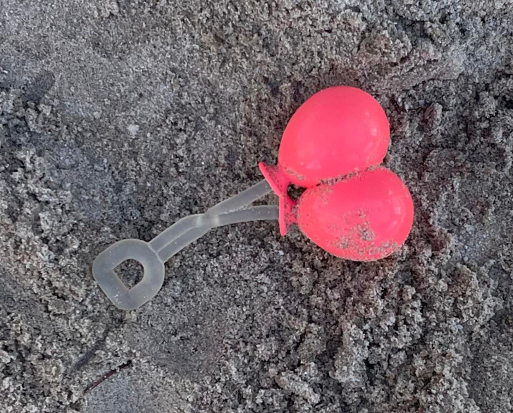 A pink balloon shaped object with a clear stem on the ground in sand.