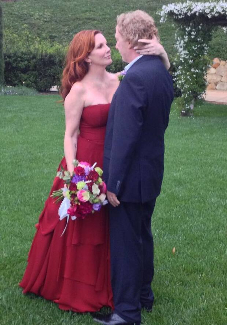 Melissa Gilbert wearing a red strapless dress and holding a bouquet looking at her husband.