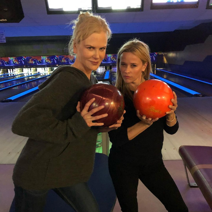 Reese Witherspoon and Nicole Kidman holding bowling balls in a bowling alley.