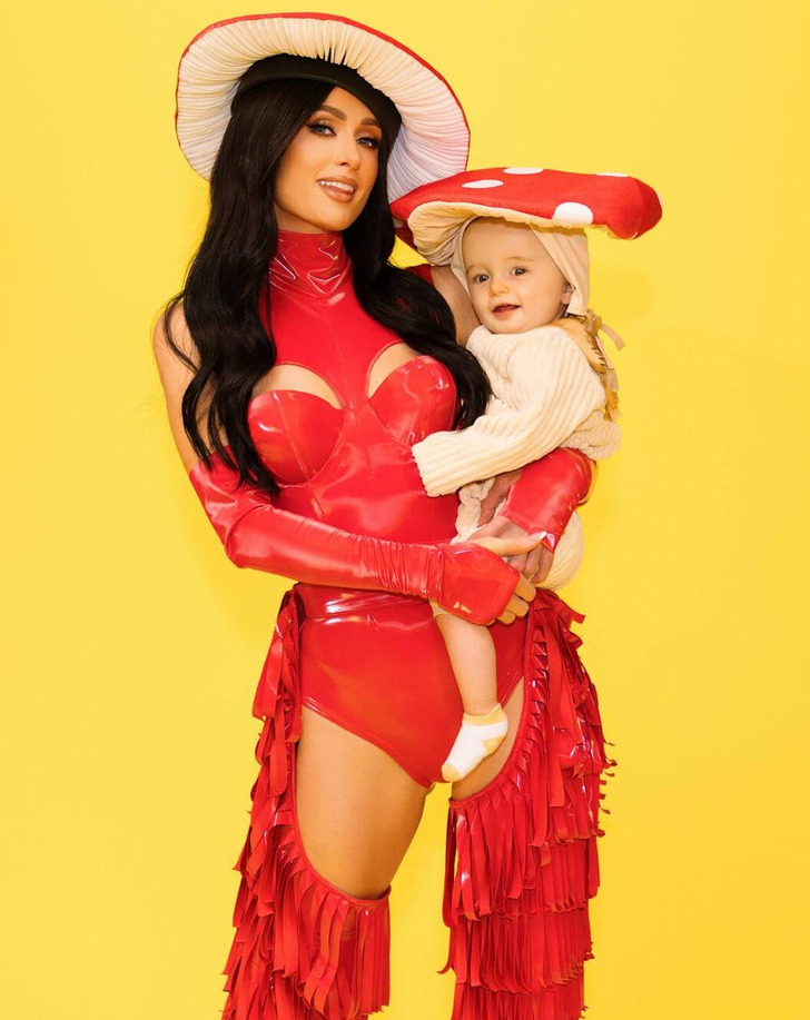 Paris Hilton in a red latex dress with cutouts above chest and on thighs, holding baby.