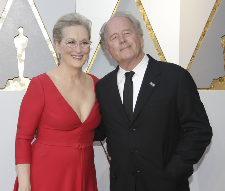 Meryl Streep and Don Gummer posing at the Oscars wearing a red dress and black suit.