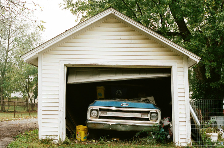 An old blue chevrolet inside a white garage with open shutter.