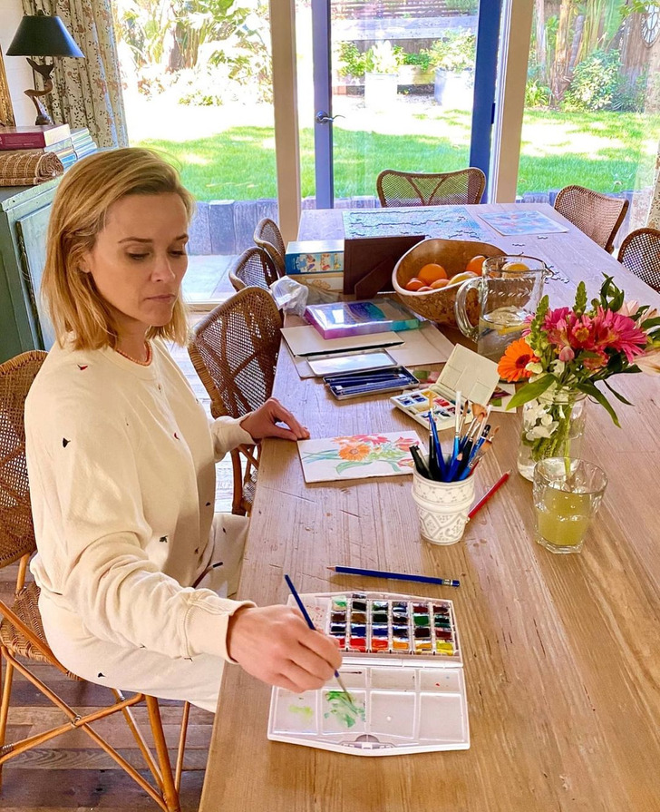 Reese Witherspoon sitting on a chair and painting.