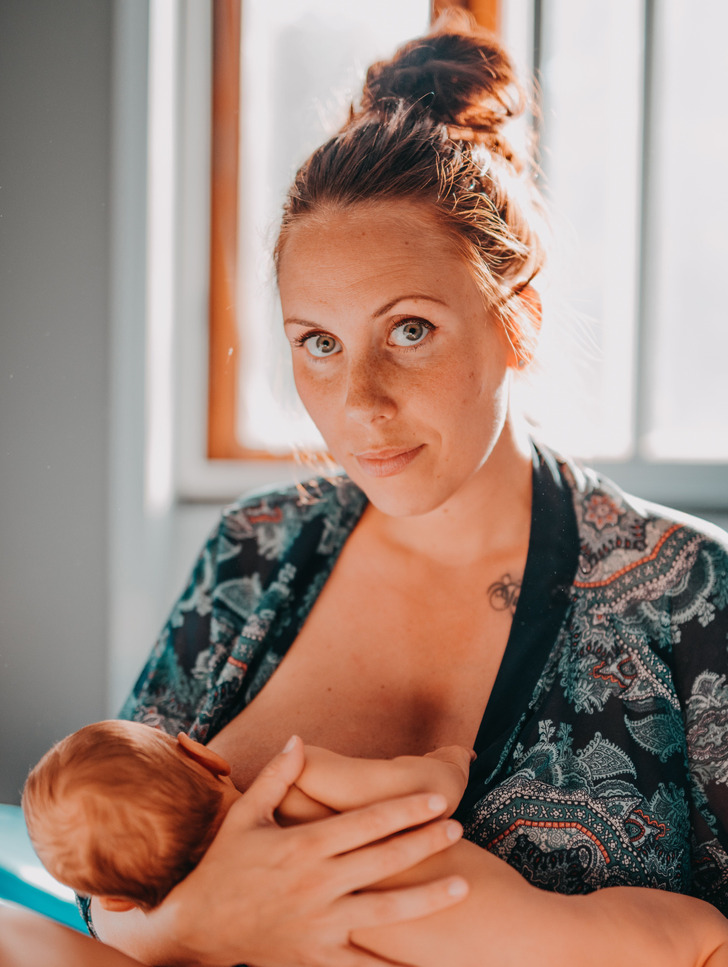 A middle aged woman in a bun breastfeeding a baby, holding it in her arms.