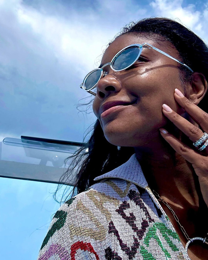 Side profile of Gabrielle Union wearing sunglasses, a sweater. and rings on a cloudy day.