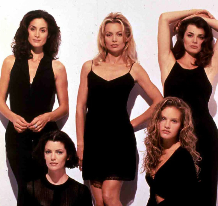 Group photo of young Carrie-Anne Moss with four other women in black dresses, posing.
