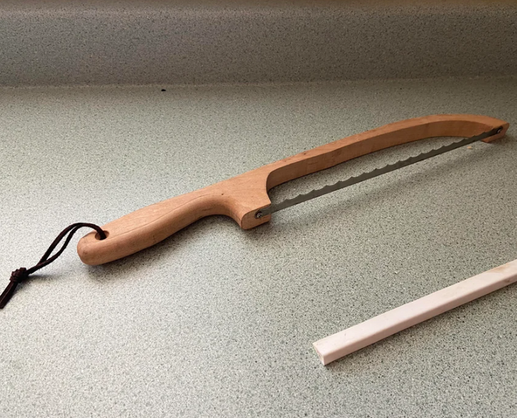 A long knife with a wooden handle kept on a marble surface.