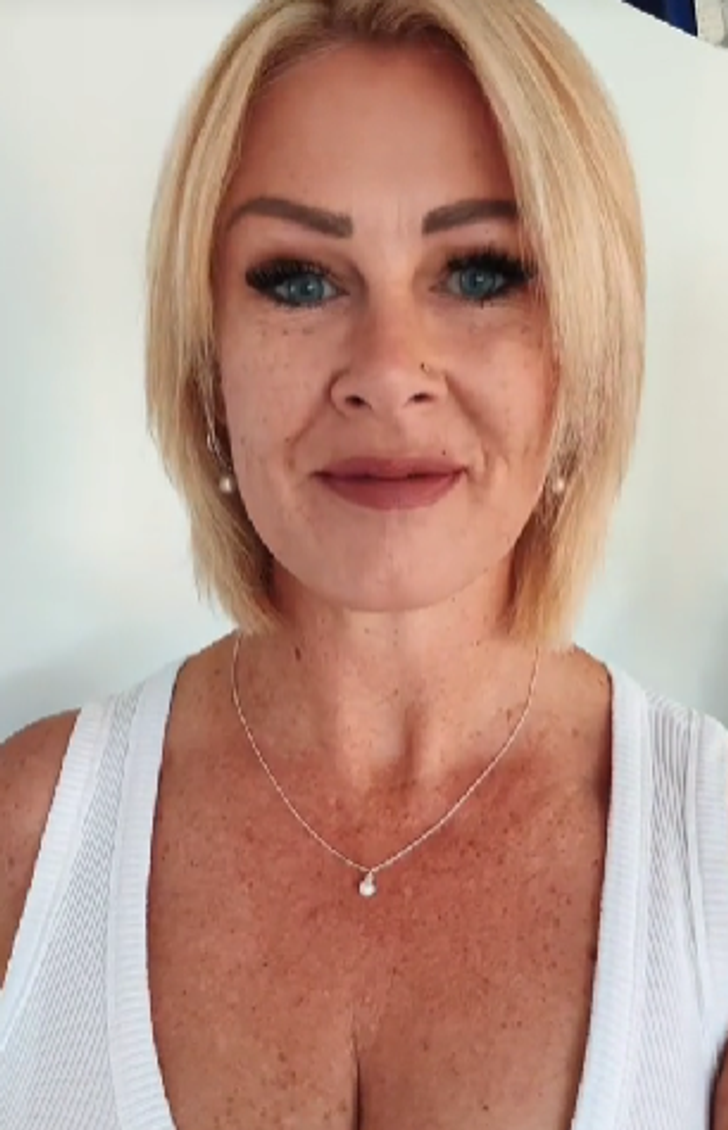 A blonde, blue eyed woman wearing a white tank top.