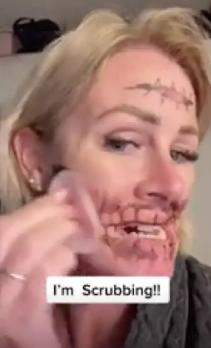 A woman removing her skull tattoo off of her face.