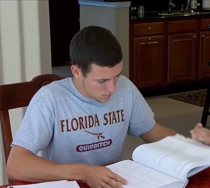 Young boy wearing a Florida State Quidditch grey t-shirt sitting and reading a book.