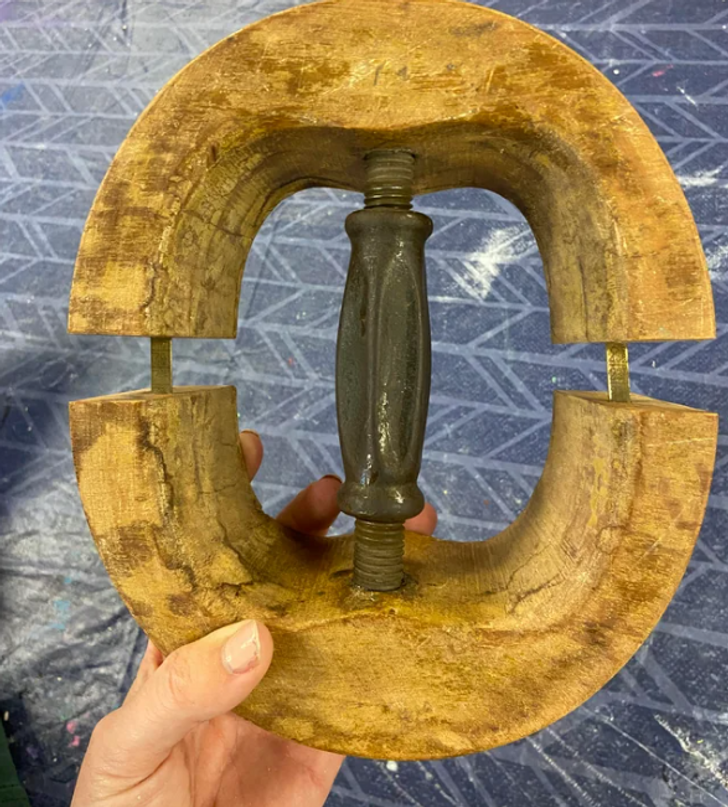 Closeup of a hand holding a large circular wooden object with a screw in middle.