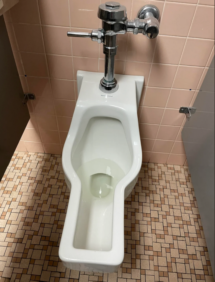 An elongated, slender urinal with a silver pipe.